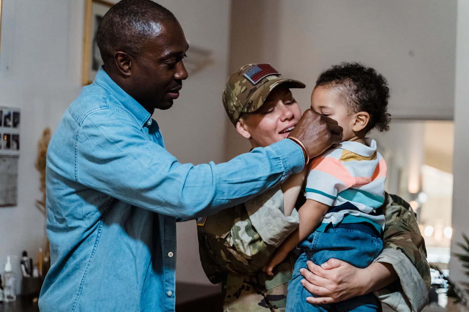 Servicewoman in Army uniform holding her young child at home while her partner reaches toward them